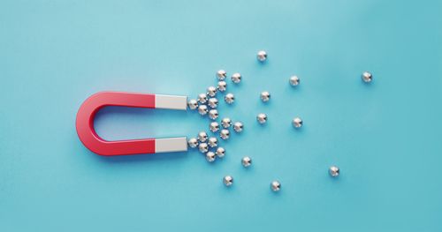 Silver Spheres Gravitated Towards a Red Magnet on Blue Background