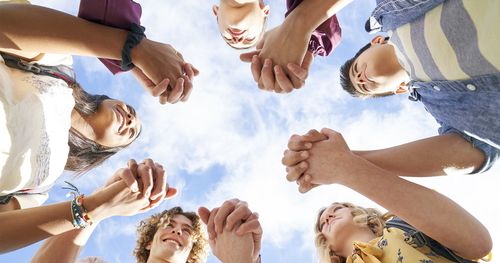 A group of young men and young women hold each other’s hands in a circle and smile at each other to encourage one another.