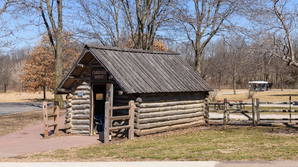 Small log building with a sign above the door that reads "Carriage Depot."