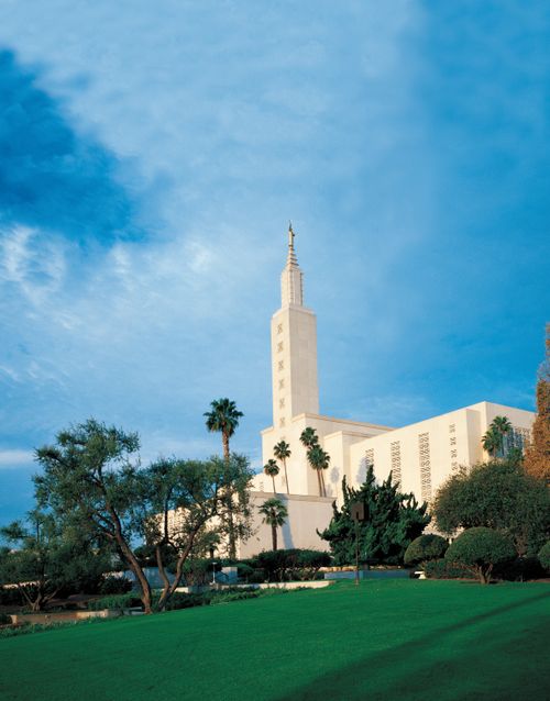 The Los Angeles California Temple seen from a distance on a sunny day, with different varieties of trees growing across the grounds.