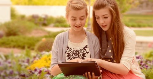 young woman helping girl with tablet