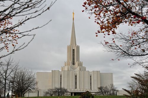 The Jordan River Utah Temple on a gray fall day, with an orange tree to the top right of the frame.