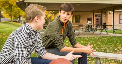 Two young men are talking to each other. They are seated outside.