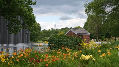 A field of colorful flowers with a white fence and red brick building. A large white temple sits in the background. 