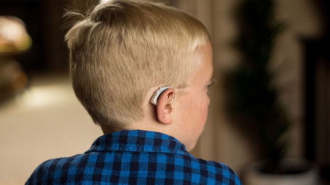 A boy wearing hearing aids is sitting and looking off to the side.