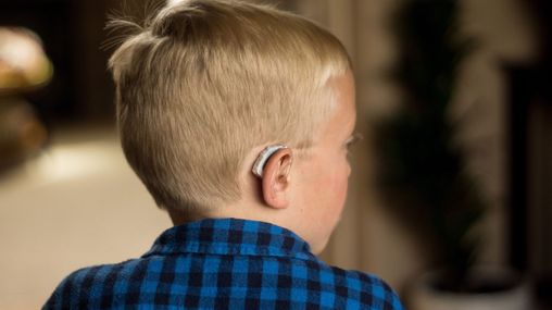 A boy wearing hearing aids is sitting and looking off to the side.