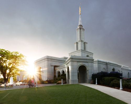 The entire Sacramento California Temple, with the sun setting in the background and a view of the grounds around the temple.