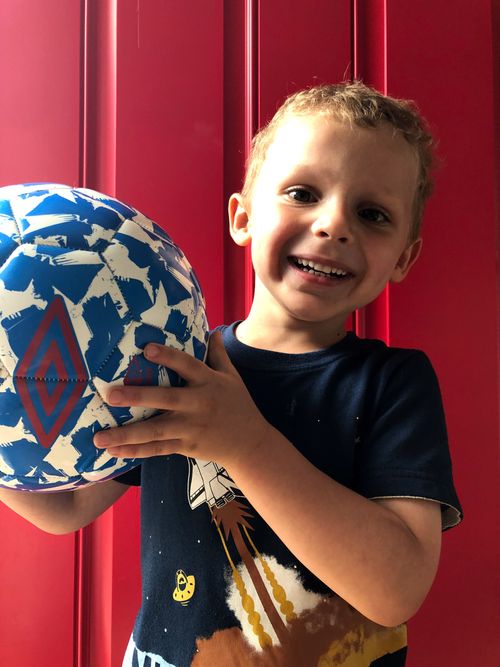 A young boy named Mark Sears holds up a soccer ball and smiles.