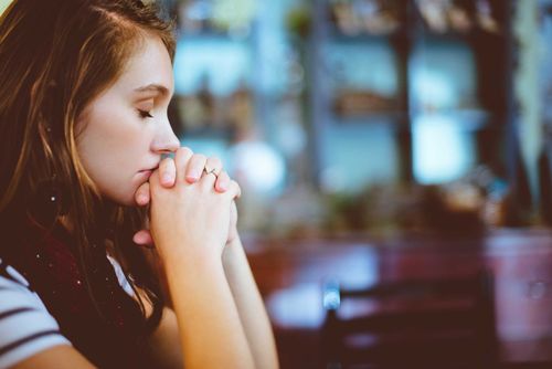 A woman folds her hands and prays.