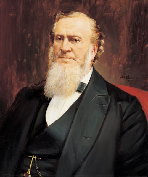 A painted portrait by John Mulvany of Brigham Young in a black suit, sitting in a red chair.
