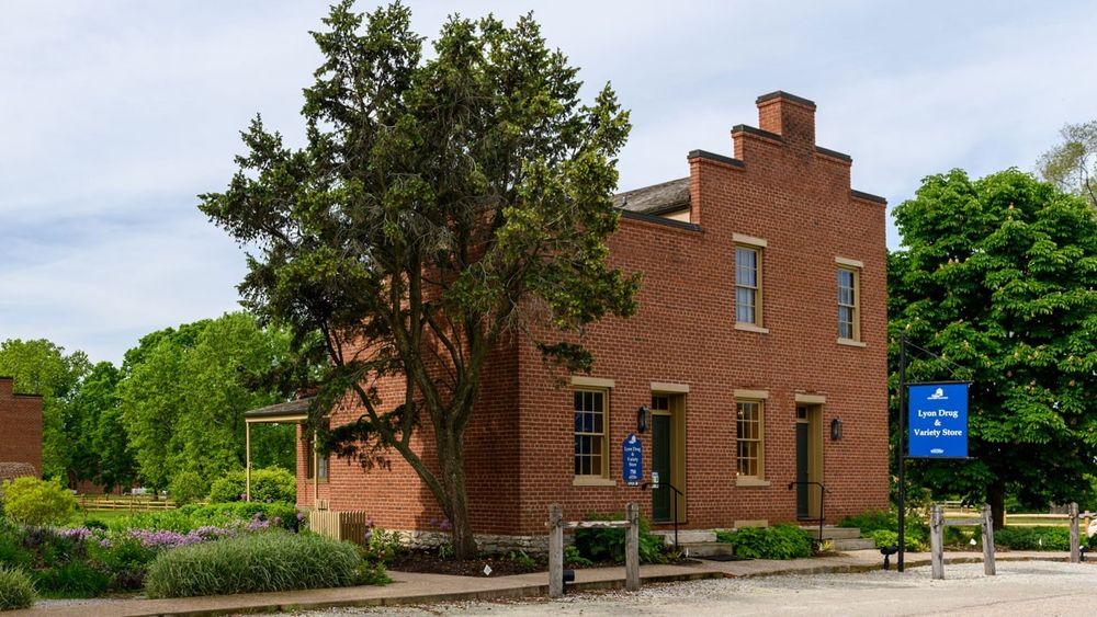 Two-story red brick building with large trees and a garden to the side.