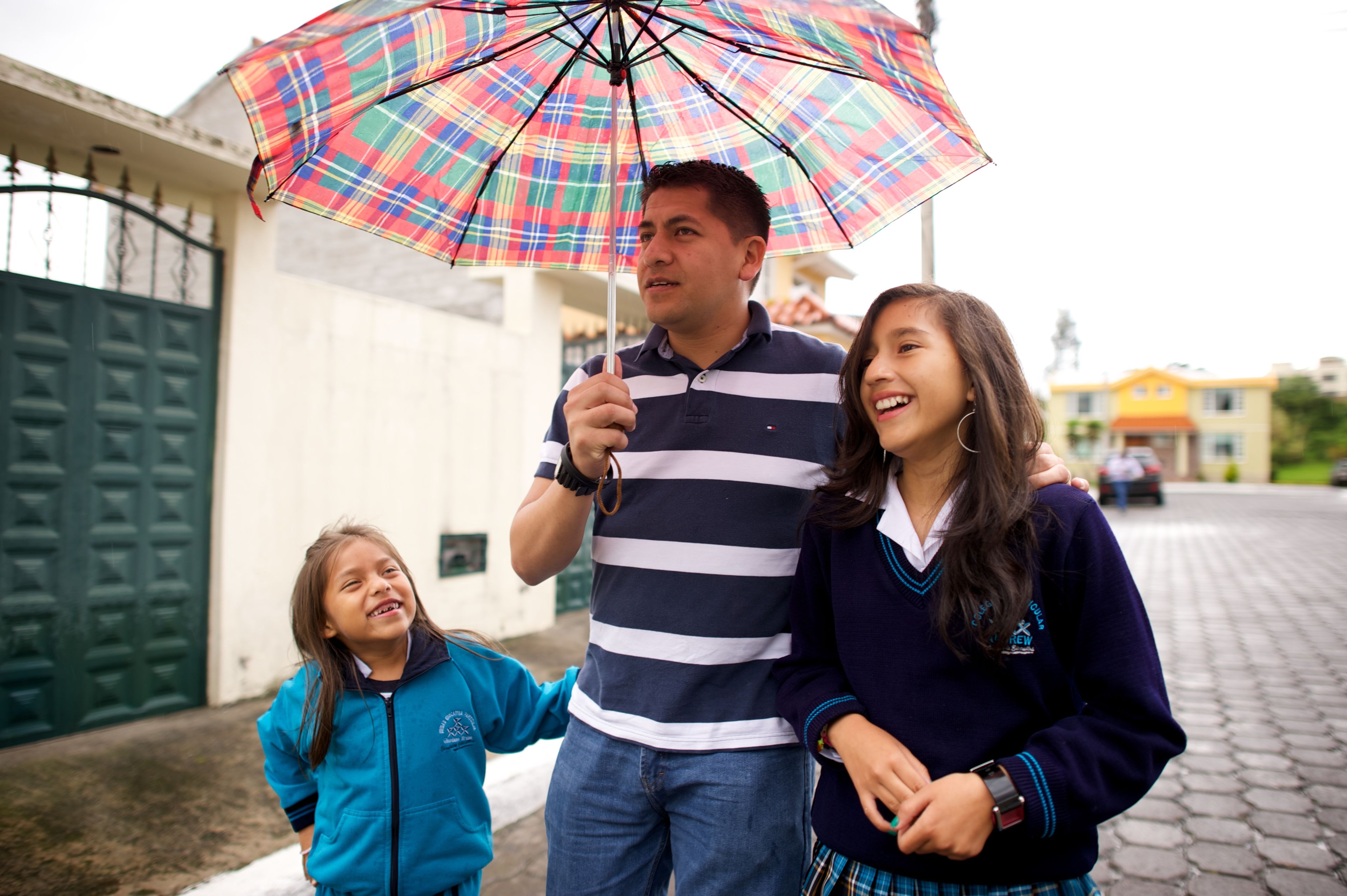 A father and two daughters walk down the road under an umbrella.