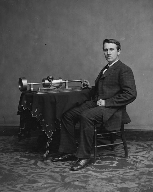 Black and White photo of Thomas Edison sitting next to the phonograph he created.