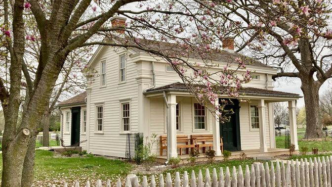 A farmhouse painted off-white with magnolia blossoms in foreground.