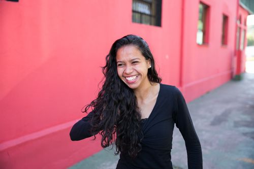 Brazil.  Portrait of a laughing woman standing against a pink wall.
