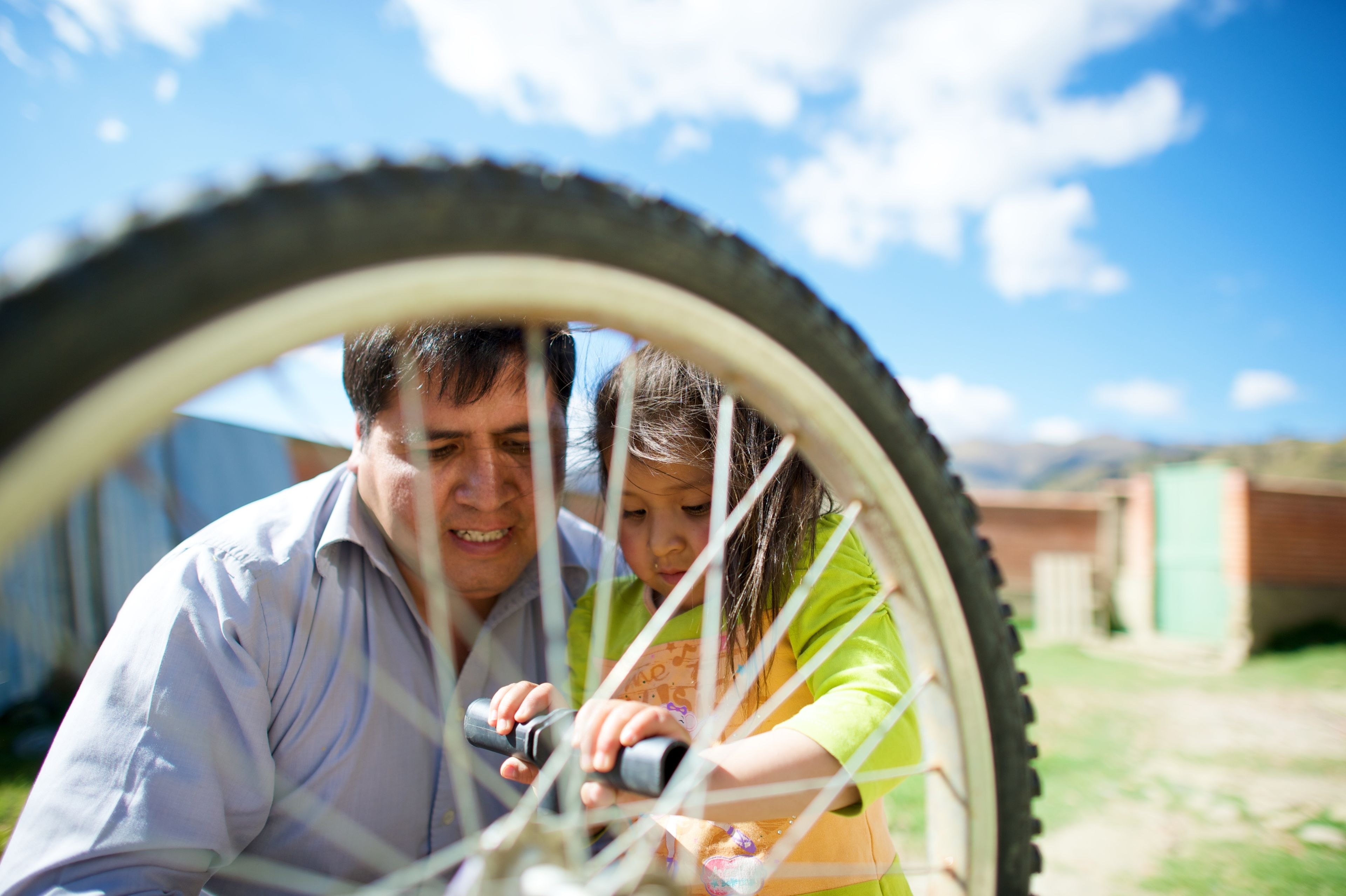 A man and his daughter sit outside and fix a bike together.