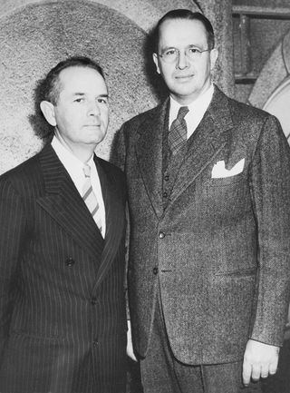 Ezra Taft Benson standing beside Spencer W. Kimball, who is wearing a black striped suit, in October 1943.