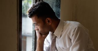 a young adult sadly looks out a window