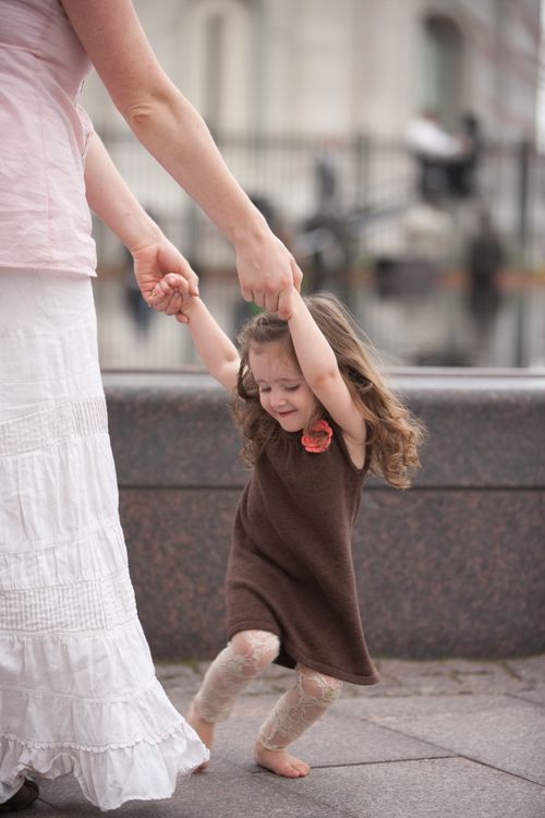 A mother in a long white skirt holding the hands of her daughter, who is dancing and smiling by the water fountain at Temple Square.