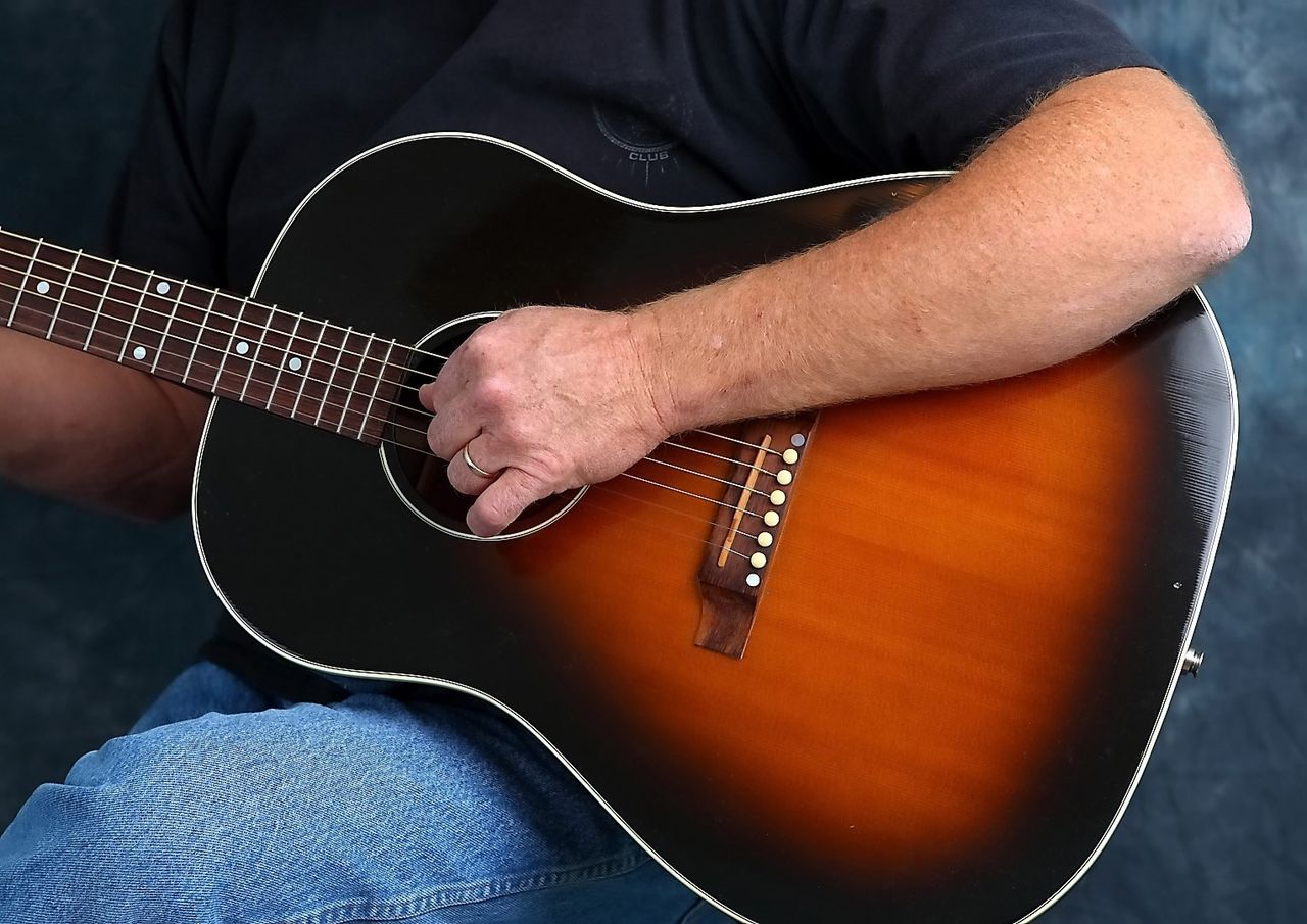 A close-up image of a man’s hand strumming the strings on a guitar.