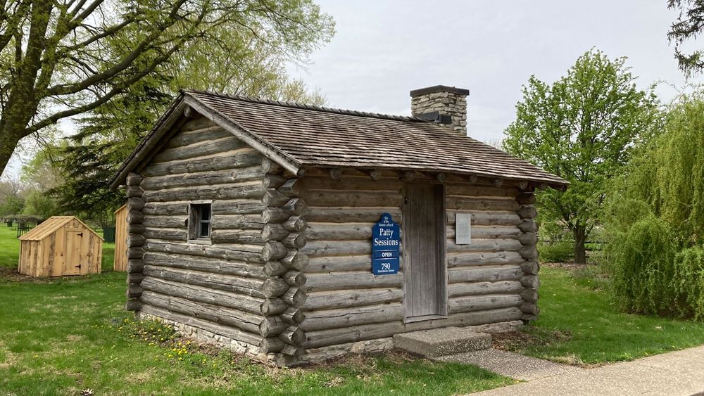 Small, one-room log cabin situated on a grass lawn.