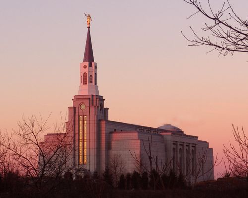 A front side view of the Boston Massachusetts Temple during sunset in the winter, with bare trees on the grounds.