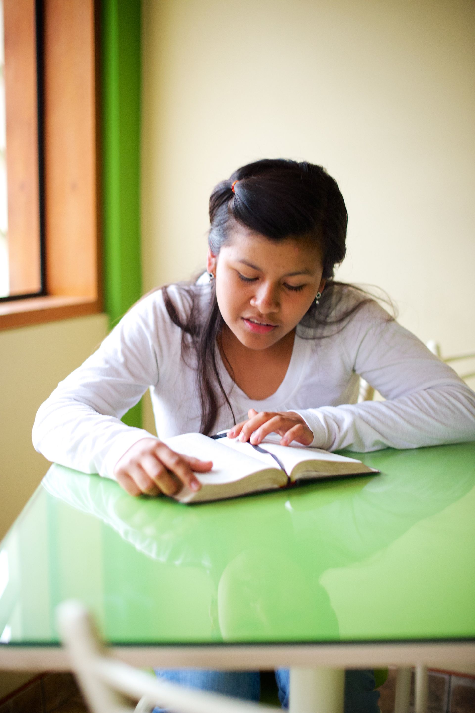 A young woman sitting at a table and reading scriptures.