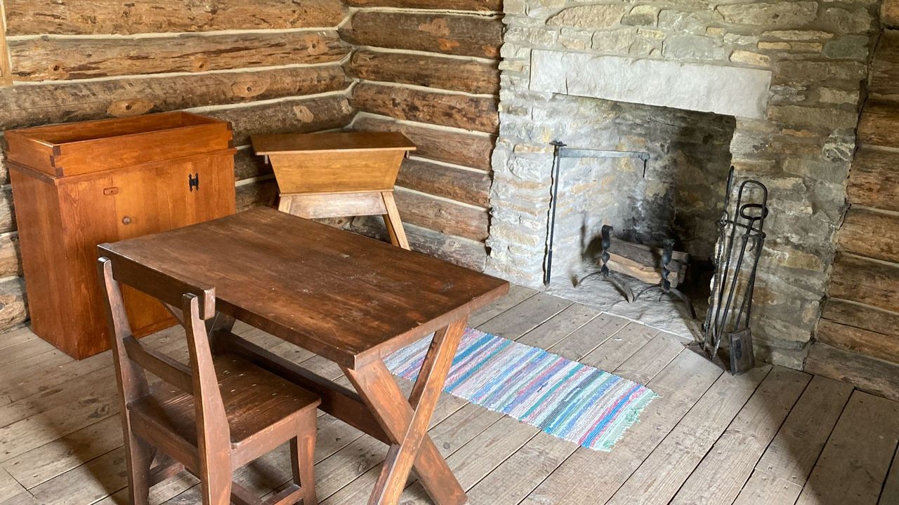 A log cabin with a small table and chair facing a stone fireplace.