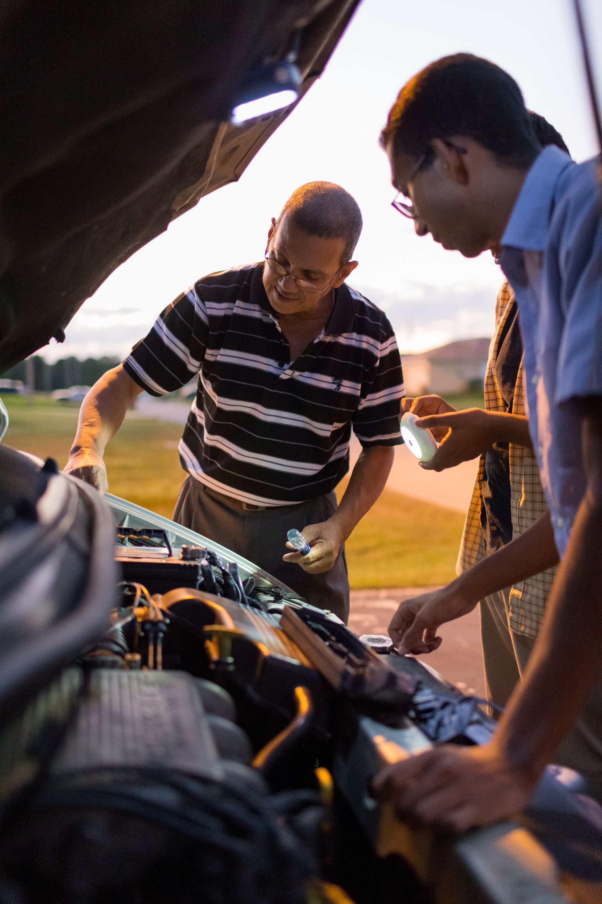 A father teaches two of his sons how to do car repairs.