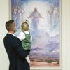 father holding his child as they look at painting of Jesus