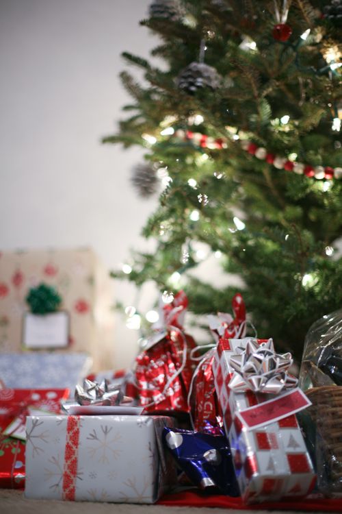 Several sizes and colors of wrapped packages sitting together beneath a lit and decorated Christmas tree.