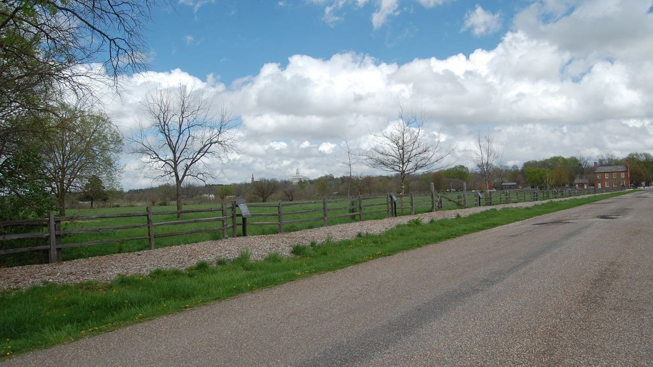 A woodchip-covered path along a tree-lined fence with interpretive waysides at regular intervals.