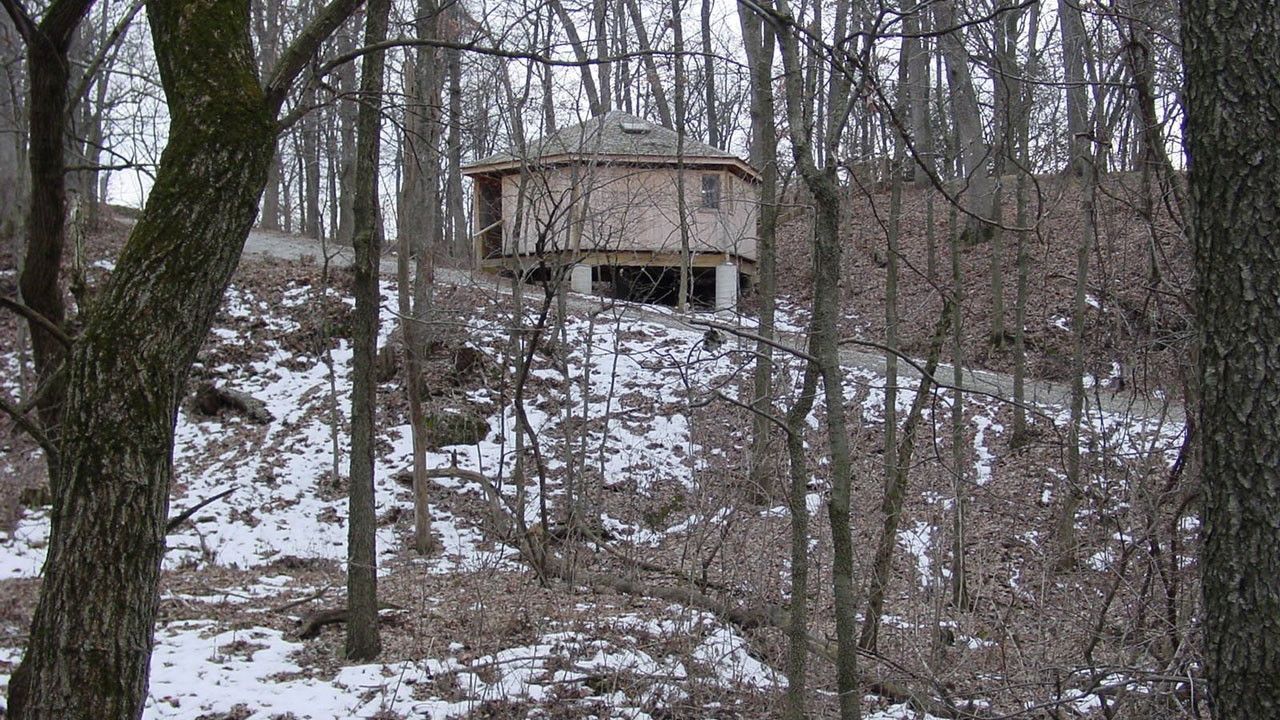 View of a octagonal kiosk through trees in the winter. There is a steep path passing in front of the kiosk.