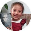 A young girls sits on a couch and smiles as she holds up a triple combination in Spanish.