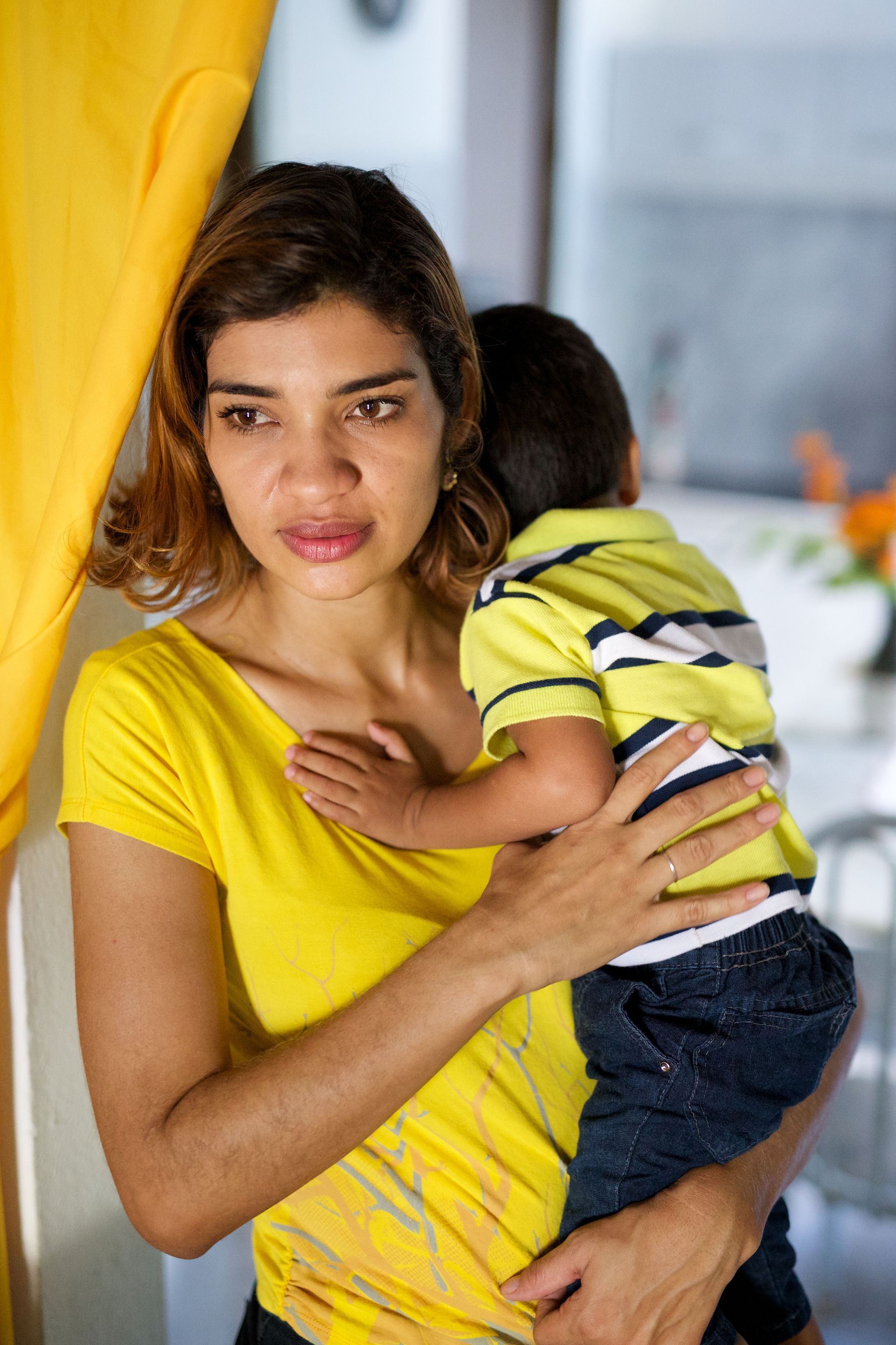 A woman holds her infant son, whose face is turned away.