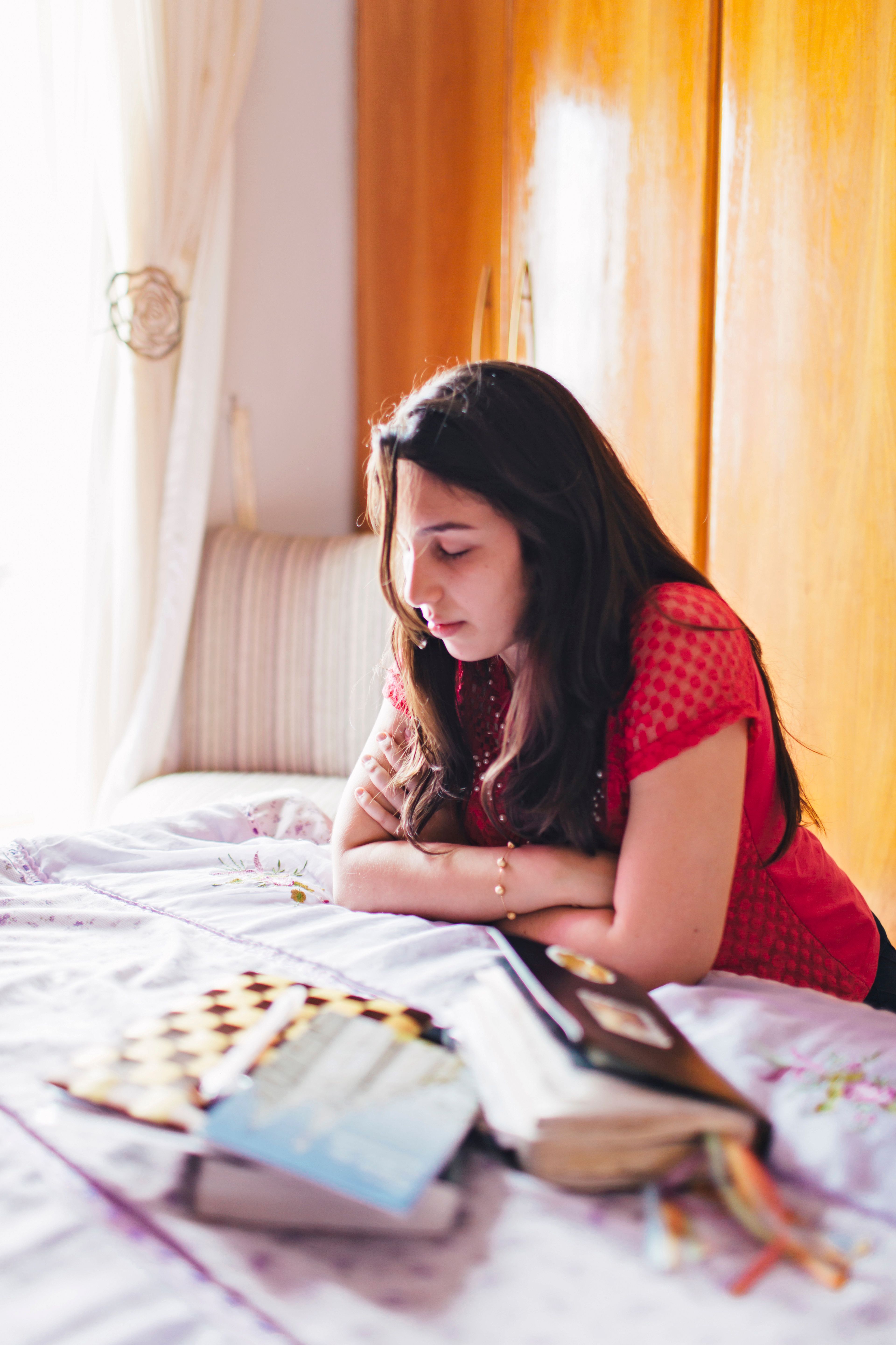 A young woman kneels by her bed and prays after reading the scriptures.