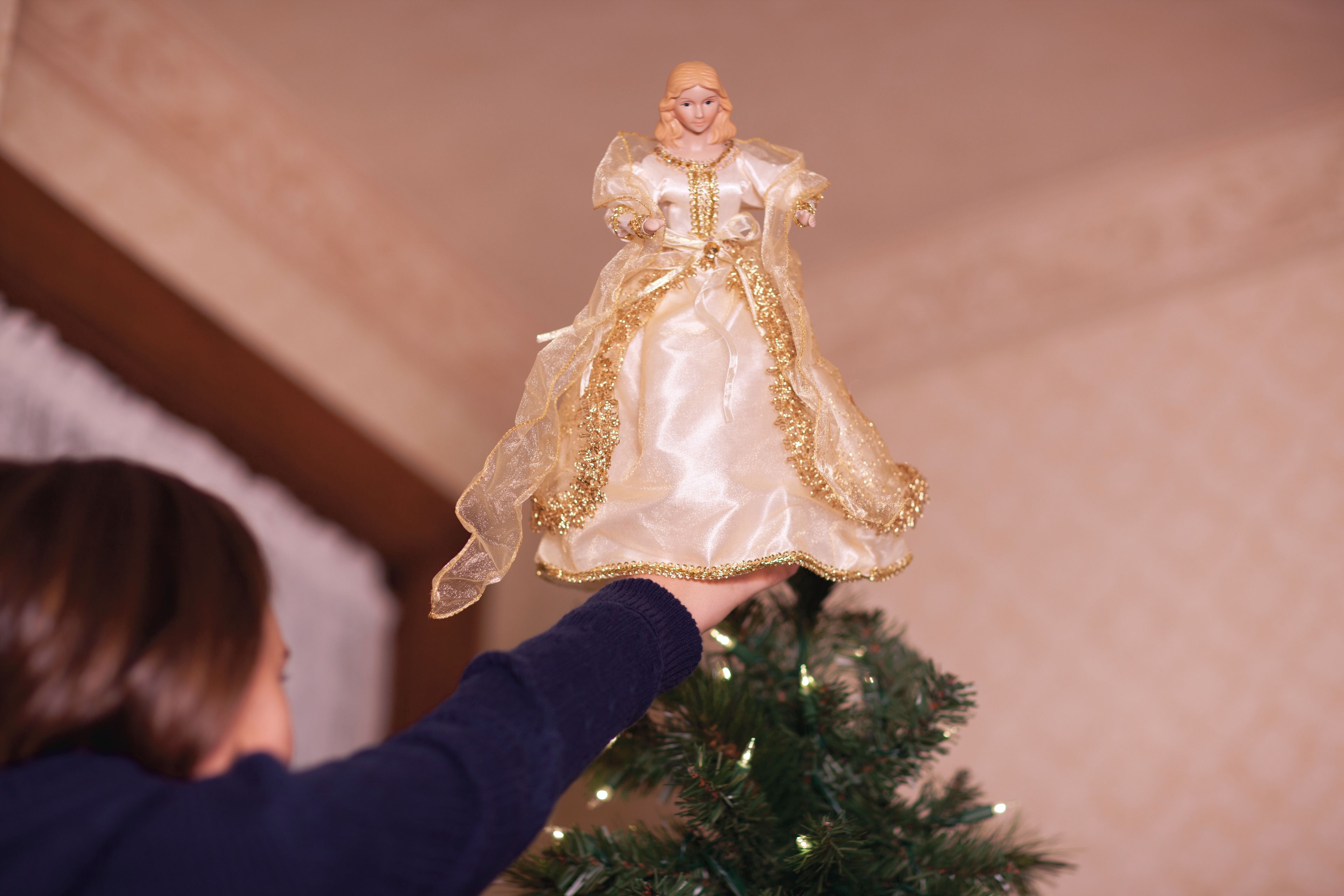 A young boy puts an angel on top of the Christmas tree.