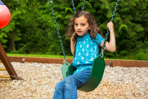 A young girl in a blue shirt and jeans swinging in a green swing.