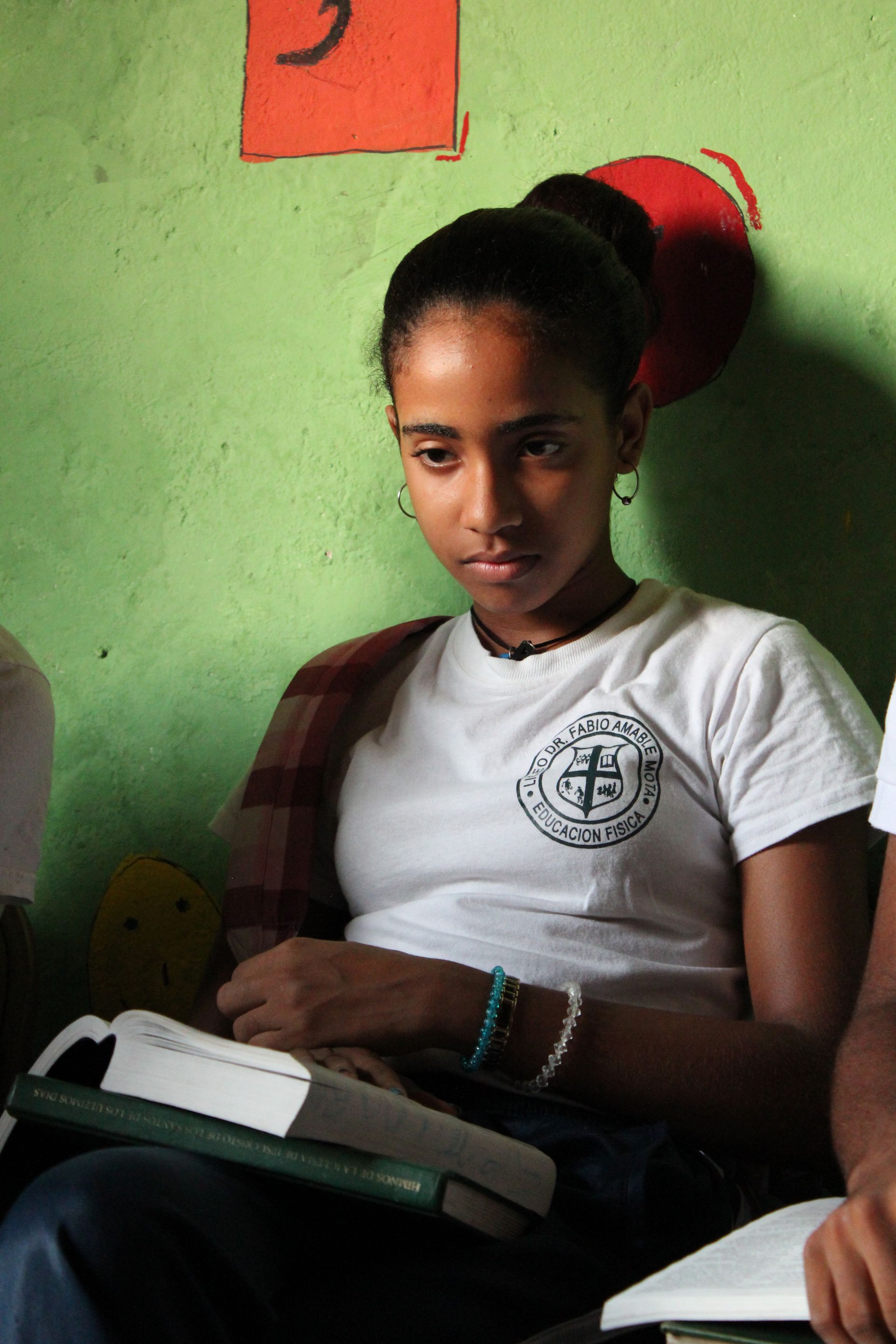 A young woman leans against a wall with her scriptures and hymnbook open on her lap during seminary.