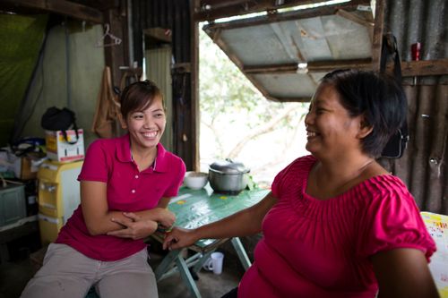 A woman and her teenage daughter, both wearing pink shirts, sit together and smile and laugh.