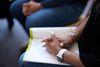 People gather together for an addiction support group. Various adults write in their workbooks. 