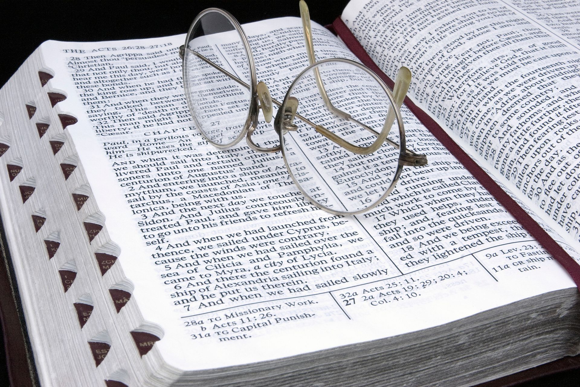 A pair of eyeglasses resting on top of a Bible, which is opened to Acts chapter 27.