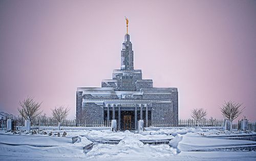 The Draper Utah Temple on a dark snowy day, with a purple sky in the background and snowflakes falling in the foreground.