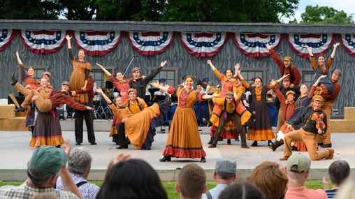 A group of performers dressed in pioneer clothing on a stage, posing after a performance.