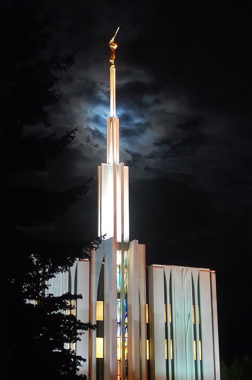 A view of the Seattle Washington Temple spire all lit up at night, with the windows on the temple lit up from inside.
