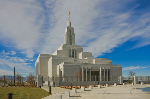 The front of the Draper Utah Temple on a sunny day, with thin white clouds overhead.