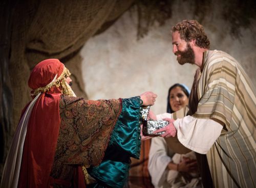 One of the Wise Men standing with outstretched arms and handing Joseph a gift while Mary stands in the background in the Arizona Christmas pageant.