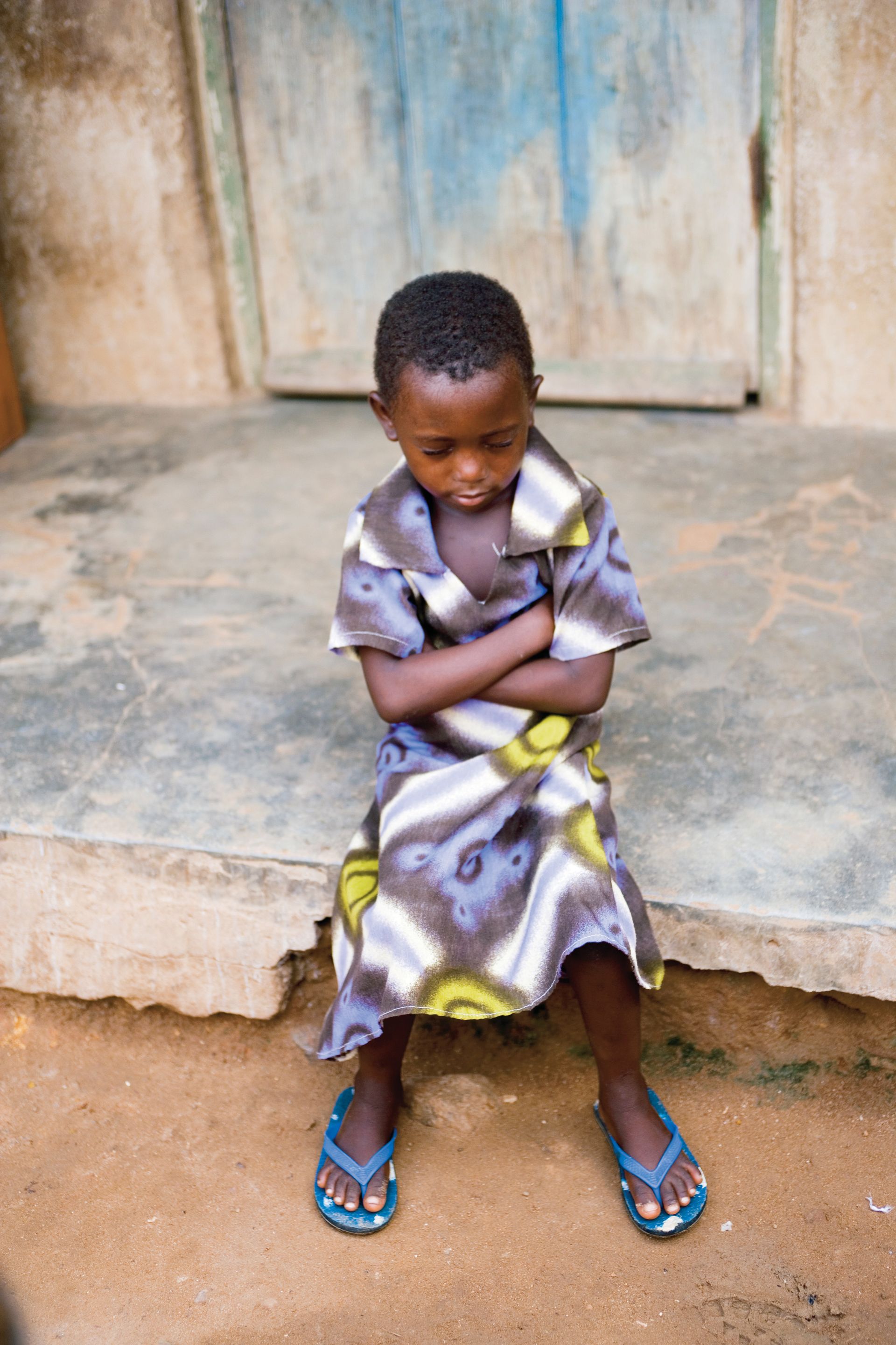 A little girl in Ghana sits on the steps and prays.