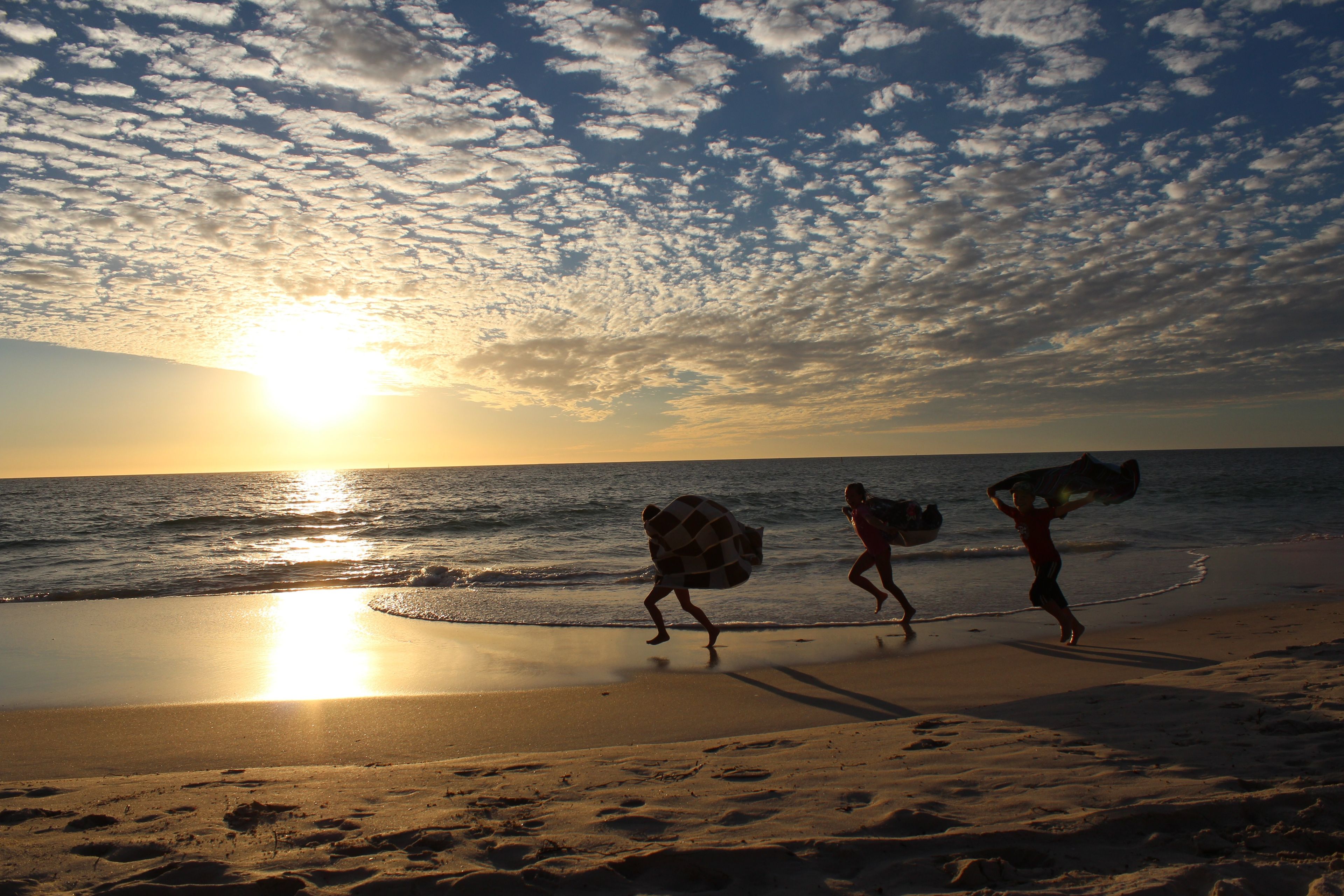 Silhouettes of three children running with towels on the beach.