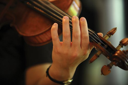 A close-up image of a woman’s hand playing on a violin.